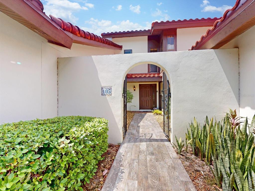 A tiled walkway leads through an arched gate to the front entrance of a house — 105 COVENTRY LANE, HAINES CITY, FL