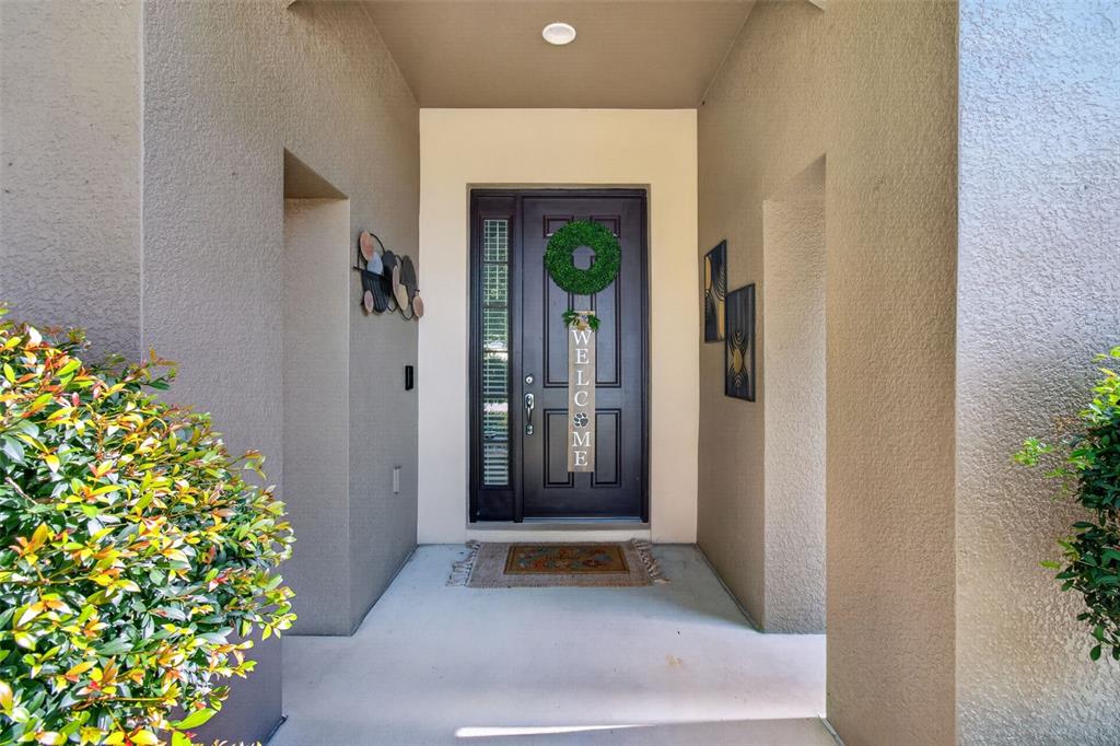 A covered entryway features a dark front door with a wreath and a welcome sign — 1234 HILL FLOWER DRIVE, BROOKSVILLE, FL