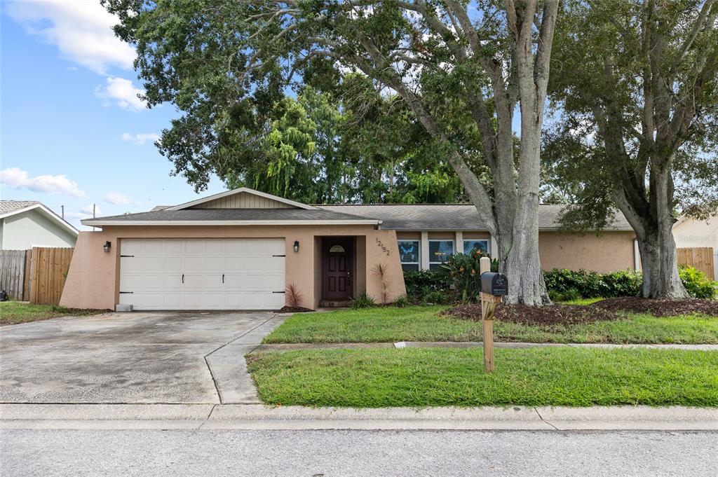 A single-story peach-colored house with a two-car garage and large trees in the front yard — 12152 BONNIE TERRACE, SEMINOLE, FL