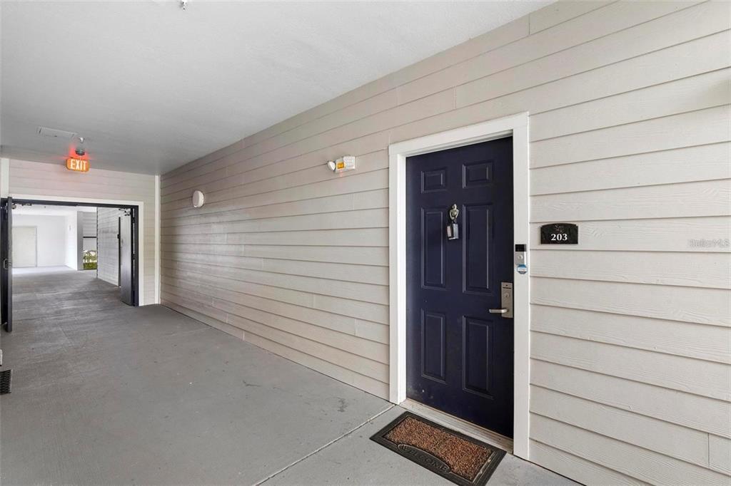 An exterior hallway features a dark blue apartment door labeled 203 with light-colored siding — 3174 FELTRIM PLACE UNIT 203, KISSIMMEE, FL