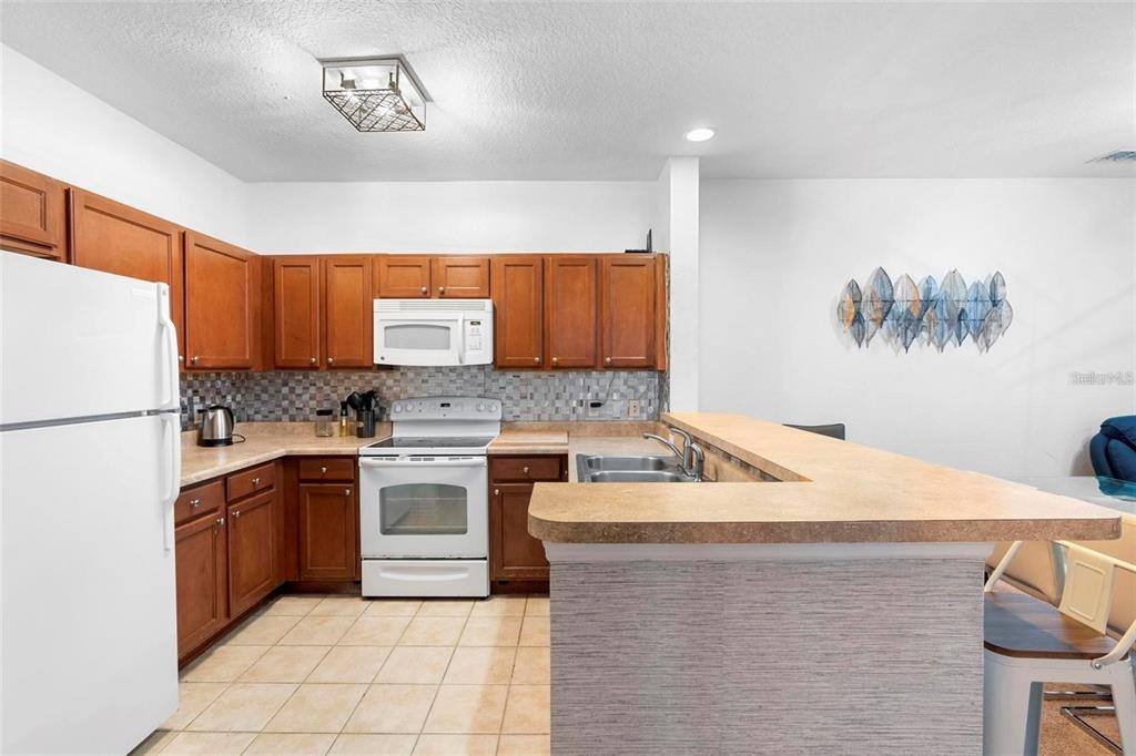 A kitchen features wood cabinets, white appliances, a tiled backsplash, and a breakfast bar counter — 3174 FELTRIM PLACE UNIT 203, KISSIMMEE, FL
