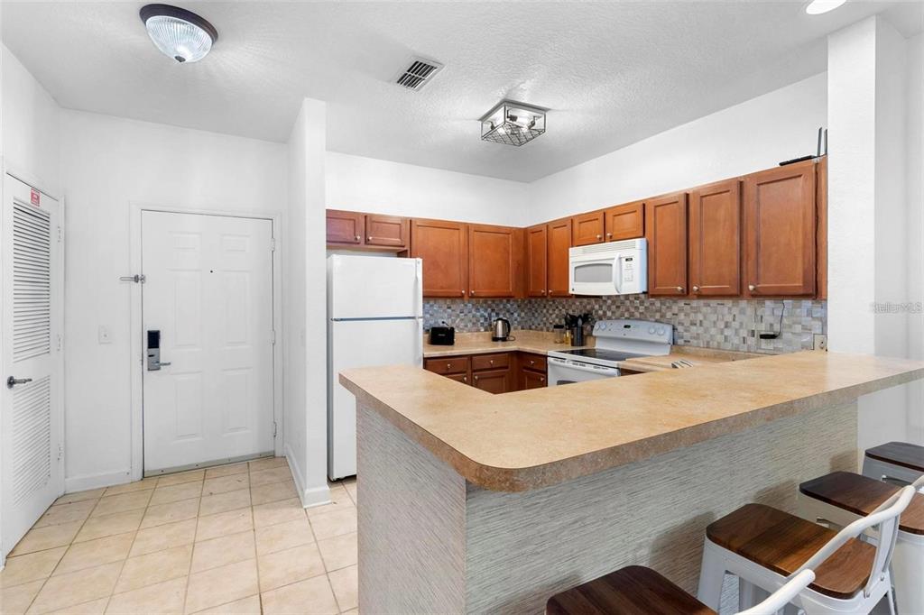 A kitchen with wood cabinets, a breakfast bar, and tile flooring — 3174 FELTRIM PLACE UNIT 203, KISSIMMEE, FL