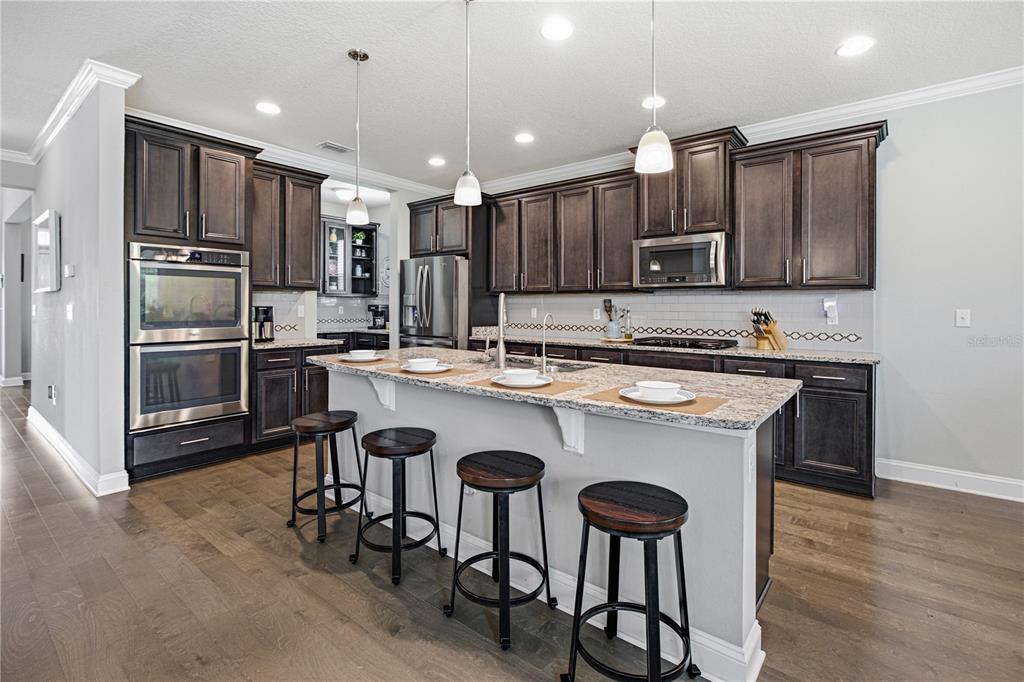 A kitchen features dark wood cabinets, granite countertops, a central island with stools, and stainless appliances — 52 CROSSWOOD COURT, ST AUGUSTINE, FL