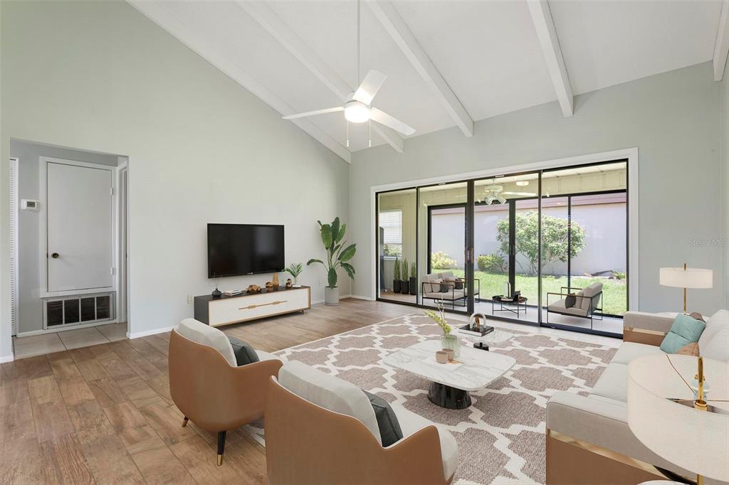 A living room features vaulted ceilings, a ceiling fan, wood-look tile flooring, and sliding glass doors — 6246 DRAW LANE UNIT 12, SARASOTA, FL