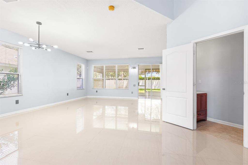 A bright, empty living room with light-colored tile floors, a modern chandelier, and sliding doors — 30419 RANDALL MANOR STREET, WESLEY CHAPEL, FL