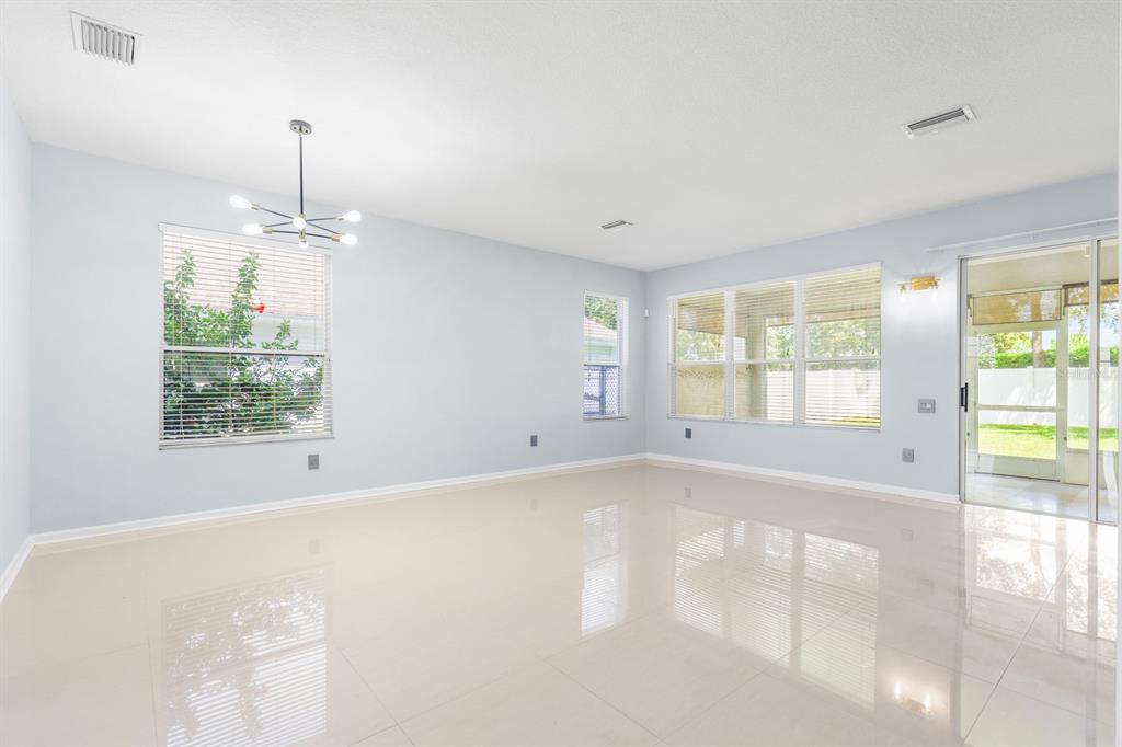 An empty room with light blue walls, tile flooring, a modern chandelier, and large windows — 30419 RANDALL MANOR STREET, WESLEY CHAPEL, FL