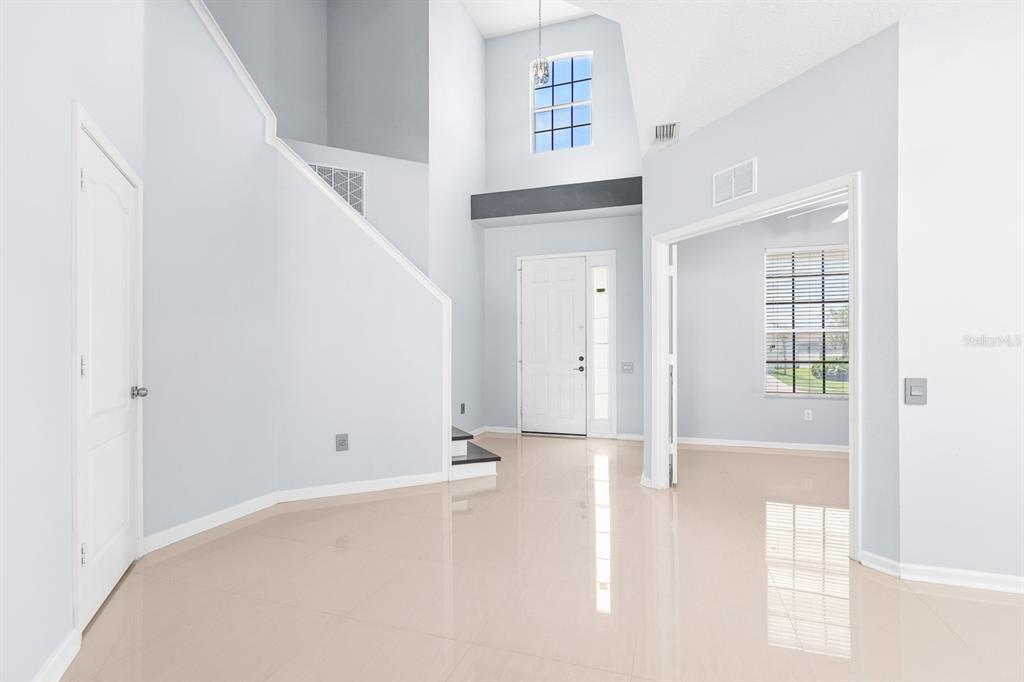 A bright, high-ceilinged foyer with light tile flooring, a white front door, and a staircase — 30419 RANDALL MANOR STREET, WESLEY CHAPEL, FL