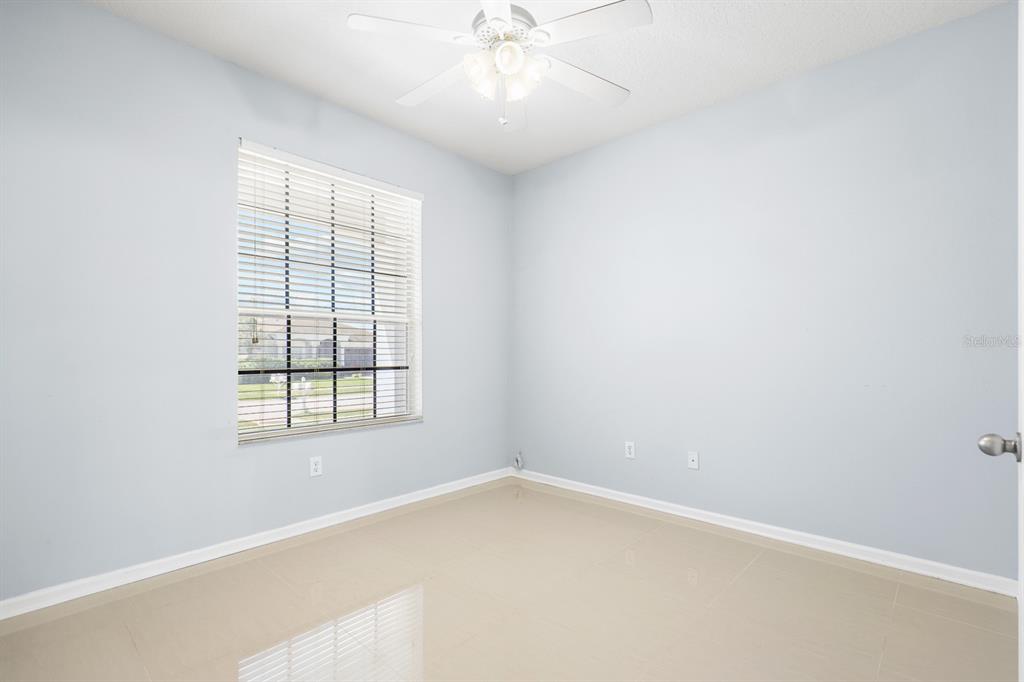 An empty room with light blue walls, tile flooring, a ceiling fan, and a window — 30419 RANDALL MANOR STREET, WESLEY CHAPEL, FL