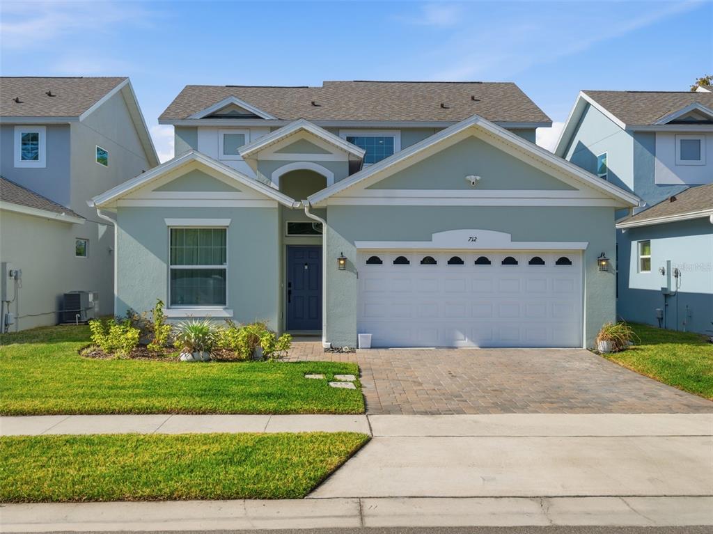 A two-story house with light green siding, a white garage door, and a paved driveway — 712 REFLECTION LAKE DRIVE, ORLANDO, FL