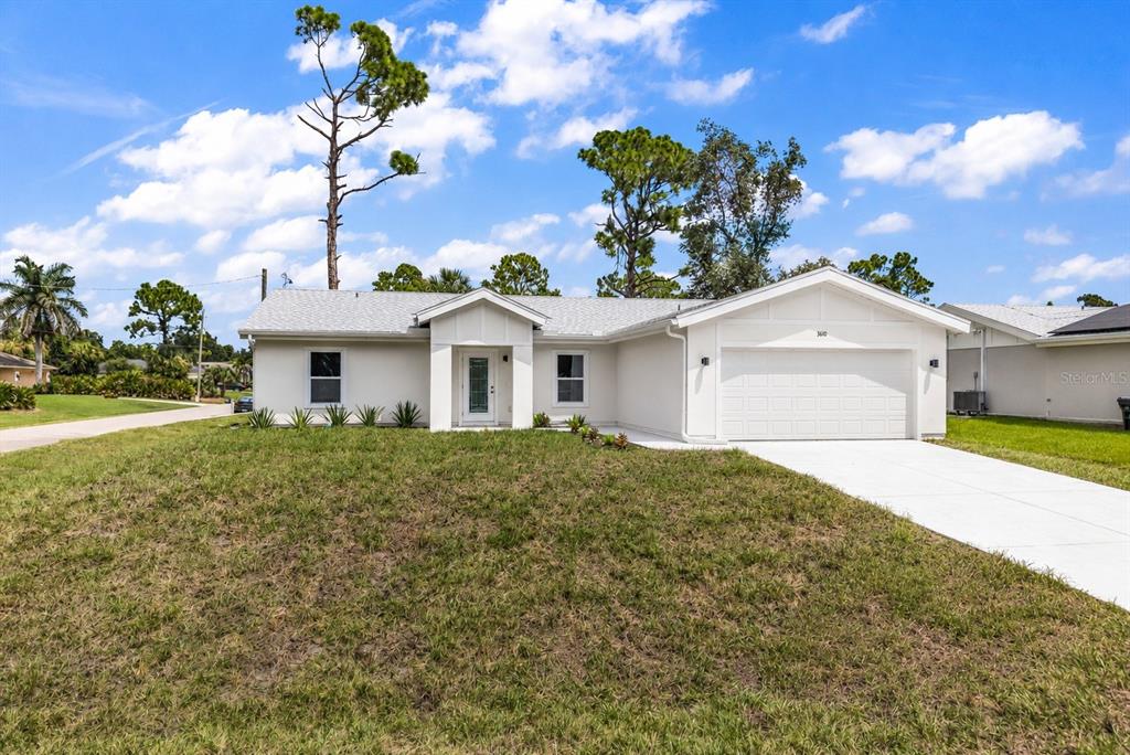 A single-story white house with a two-car garage and a front lawn under a blue sky — 3610 LAREDO AVENUE, NORTH PORT, FL