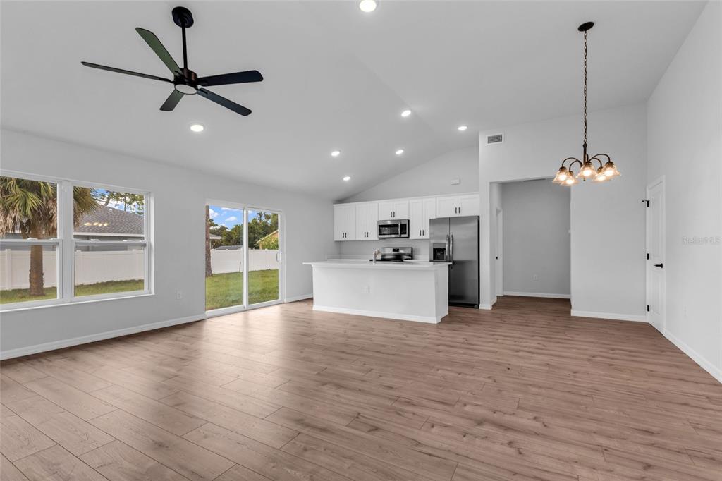An open-concept living room and kitchen with light wood flooring, white cabinets, and stainless appliances — 3610 LAREDO AVENUE, NORTH PORT, FL