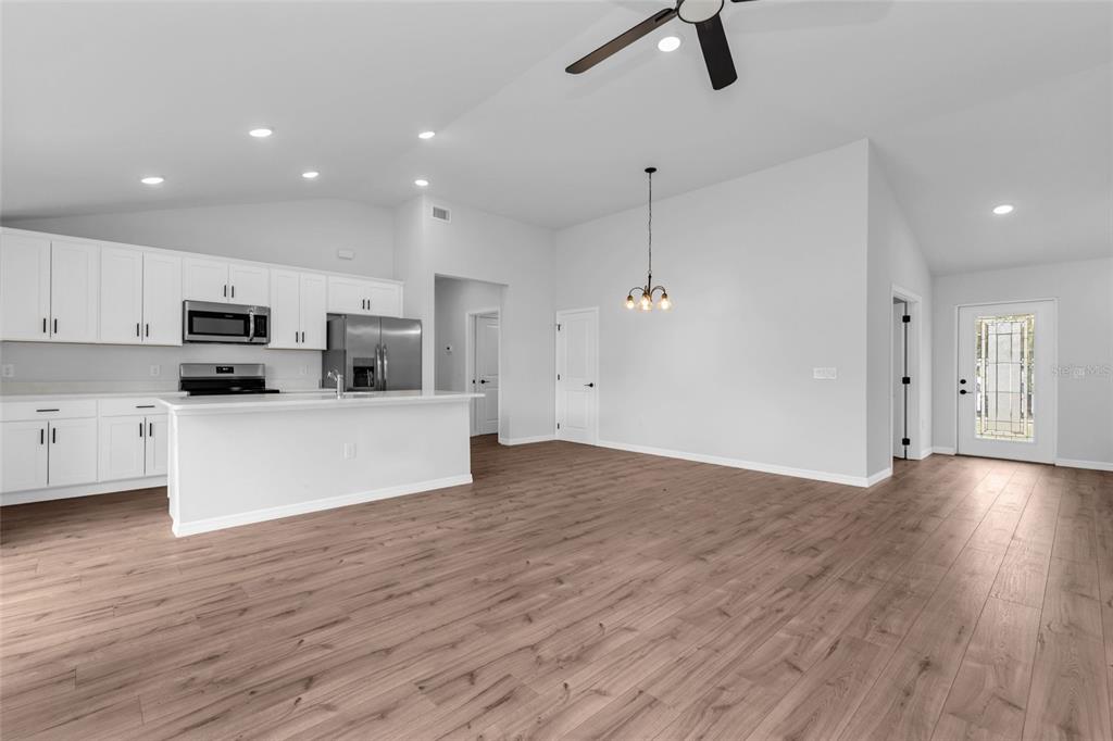 An open-concept kitchen and living area features white cabinetry, stainless steel appliances, and wood flooring — 3610 LAREDO AVENUE, NORTH PORT, FL