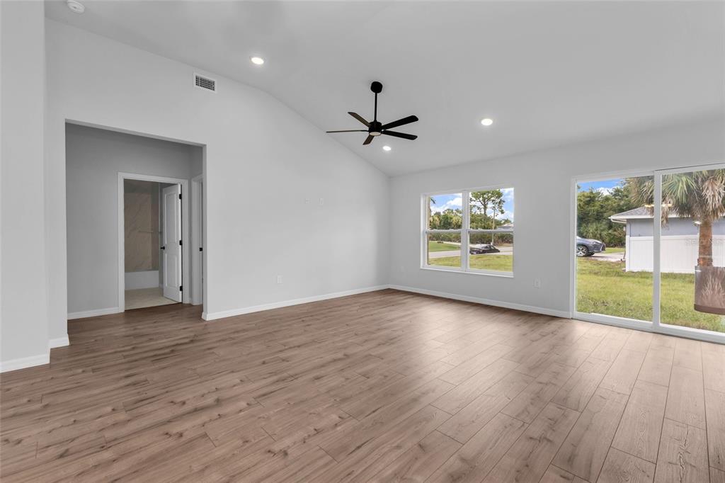An empty living room features light wood-look flooring, a vaulted ceiling, and a sliding glass door — 3610 LAREDO AVENUE, NORTH PORT, FL