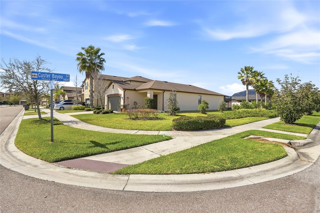 A single-story house with a tan exterior sits on a corner lot with palm trees — 1724 PASSAGE KEY LANE, RUSKIN, FL