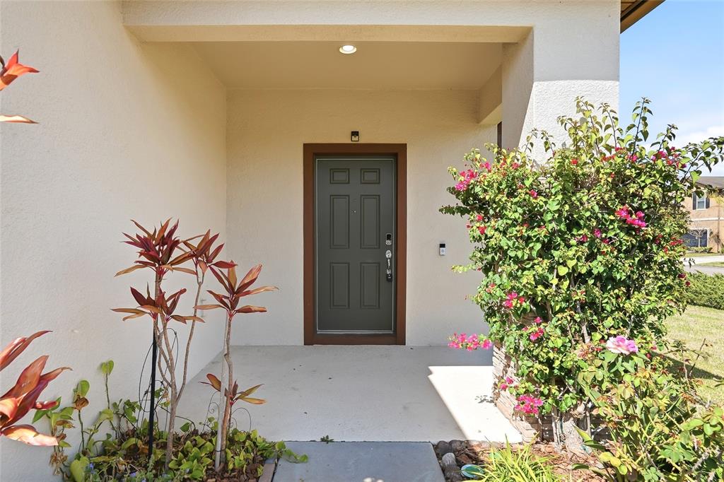 A covered front porch features a dark gray door and a large flowering bush — 1724 PASSAGE KEY LANE, RUSKIN, FL