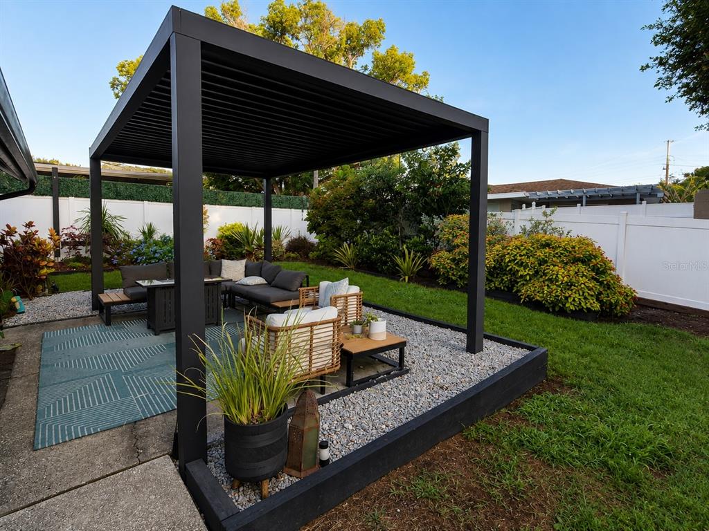 A black pergola covers a gravel patio area with outdoor seating in a backyard — 1504 BIG BASS DRIVE, TARPON SPRINGS, FL