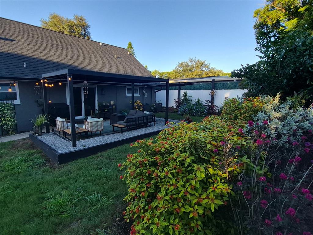 A backyard patio features a black pergola, gravel flooring, and outdoor furniture near a house — 1504 BIG BASS DRIVE, TARPON SPRINGS, FL