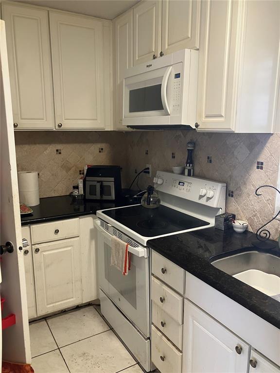 A kitchen features white cabinets, black countertops, a white stove, and a built-in microwave — 316 N BAYSHORE BOULEVARD UNIT 105, CLEARWATER, FL