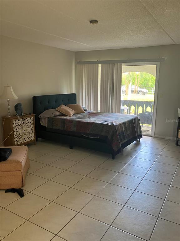 A bedroom features a dark upholstered bed, tile flooring, and a sliding glass door — 316 N BAYSHORE BOULEVARD UNIT 105, CLEARWATER, FL