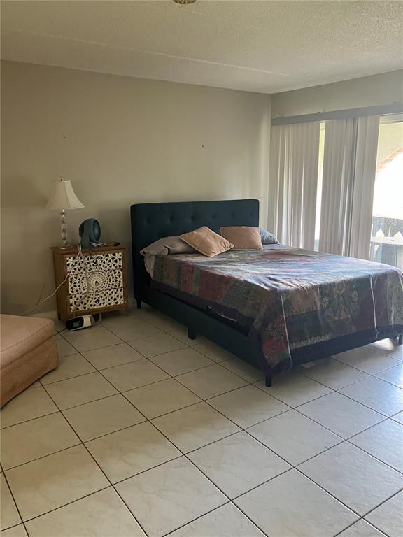 A bedroom features a dark upholstered bed, a decorative nightstand, and light-colored tile flooring — 316 N BAYSHORE BOULEVARD UNIT 105, CLEARWATER, FL