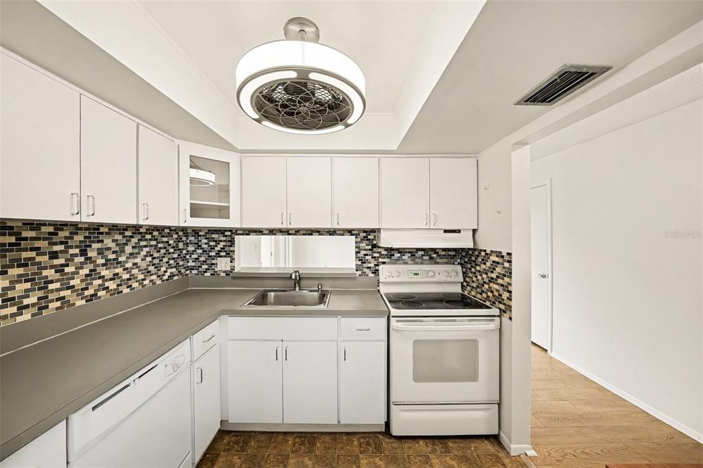 A kitchen features white cabinets, a mosaic tile backsplash, gray countertops, and a ceiling fan — 513 POLARIS LOOP UNIT 101, CASSELBERRY, FL