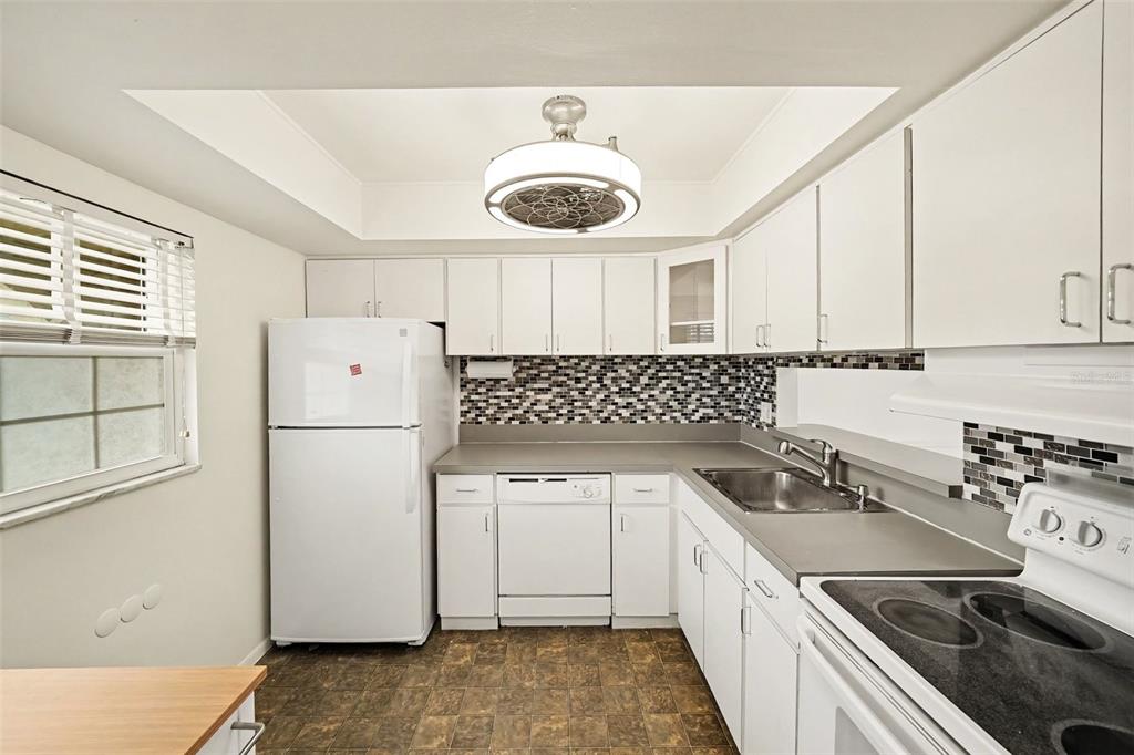A kitchen features white cabinets, a mosaic tile backsplash, white appliances, and a ceiling fan — 513 POLARIS LOOP UNIT 101, CASSELBERRY, FL