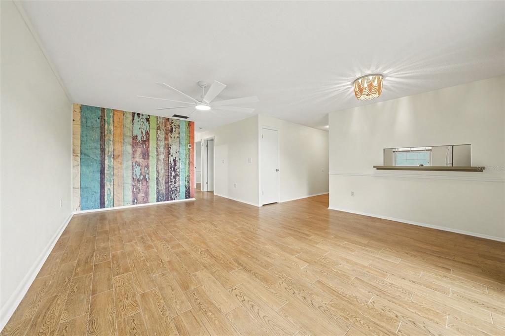 A living room with light wood-look tile flooring, a ceiling fan, and a rustic accent wall — 513 POLARIS LOOP UNIT 101, CASSELBERRY, FL