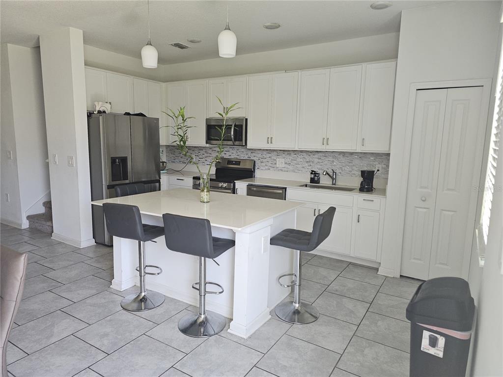 A kitchen features white cabinets, a central island with three stools, and stainless steel appliances — 3166 LAURENT LOOP, DAVENPORT, FL
