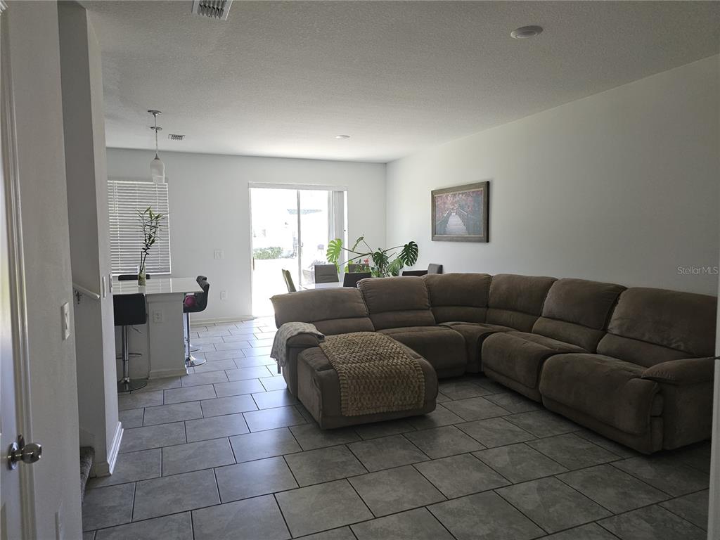 A living room with tile flooring and a large sectional sofa opens to a kitchen — 3166 LAURENT LOOP, DAVENPORT, FL