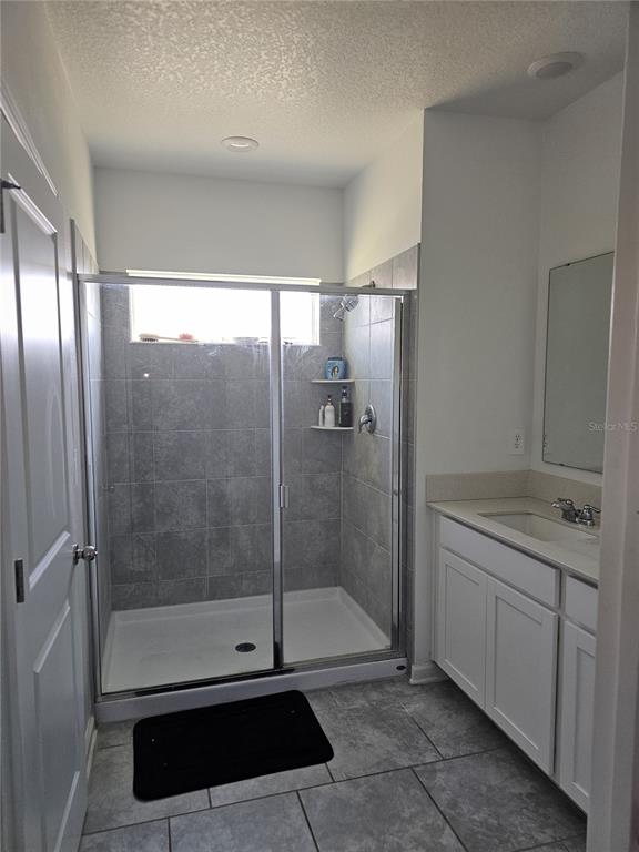 A bathroom features a tiled walk-in shower, a white vanity, and gray floor tiles — 3166 LAURENT LOOP, DAVENPORT, FL