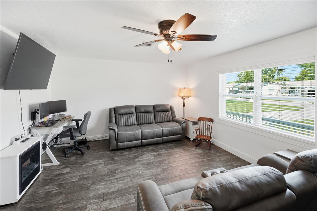 A living room with gray wood-look flooring, a gray sofa, a desk, and a ceiling fan — 407 TENNESSEE AVENUE, ST CLOUD, FL