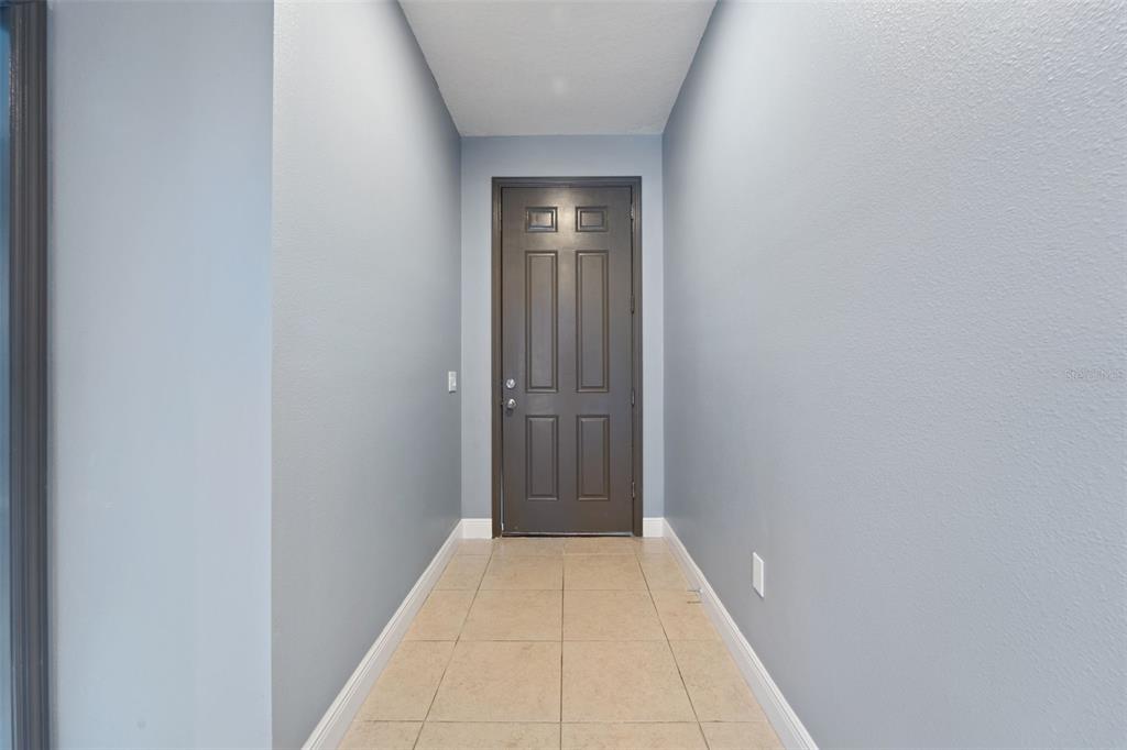 A narrow entryway features light blue walls, beige tile flooring, and a dark brown door — 11006 TAHITI ISLE LANE, TAMPA, FL