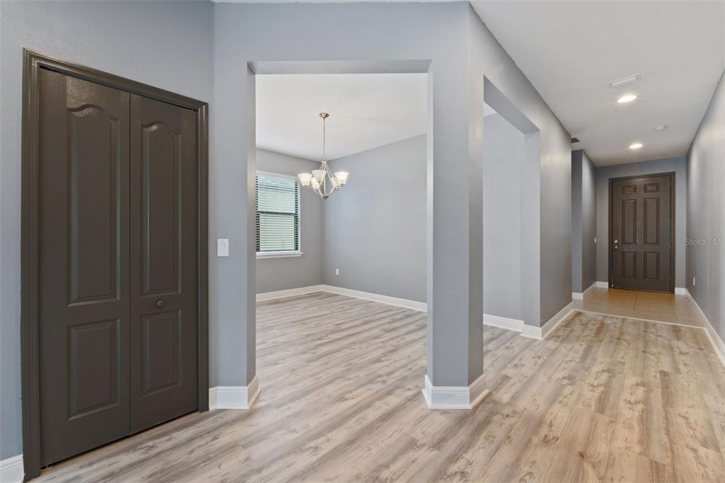 A light gray room with wood-look flooring, a chandelier, and a dark brown entry door — 11006 TAHITI ISLE LANE, TAMPA, FL