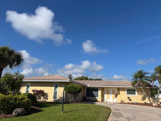 A grassy backyard features a large tree, a stone retaining wall, and a canal view — 4 WINDSOR DRIVE, ENGLEWOOD, FL