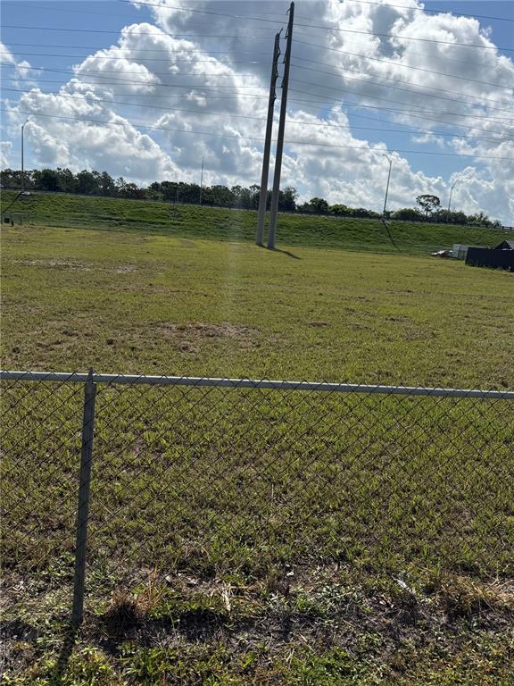 A chain-link fence borders a large, grassy vacant lot with utility poles under a cloudy sky — ECONLOCKHATCHEE TRAIL S, ORLANDO, FL