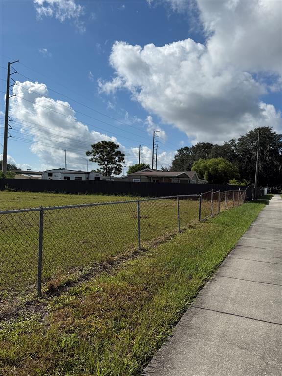 A chain-link fence borders a grassy vacant lot next to a sidewalk under a cloudy sky — ECONLOCKHATCHEE TRAIL S, ORLANDO, FL