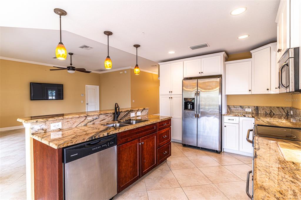A kitchen features dark wood cabinets, granite countertops, stainless steel appliances, and white upper cabinets — 3715 SEBRING PARKWAY, SEBRING, FL