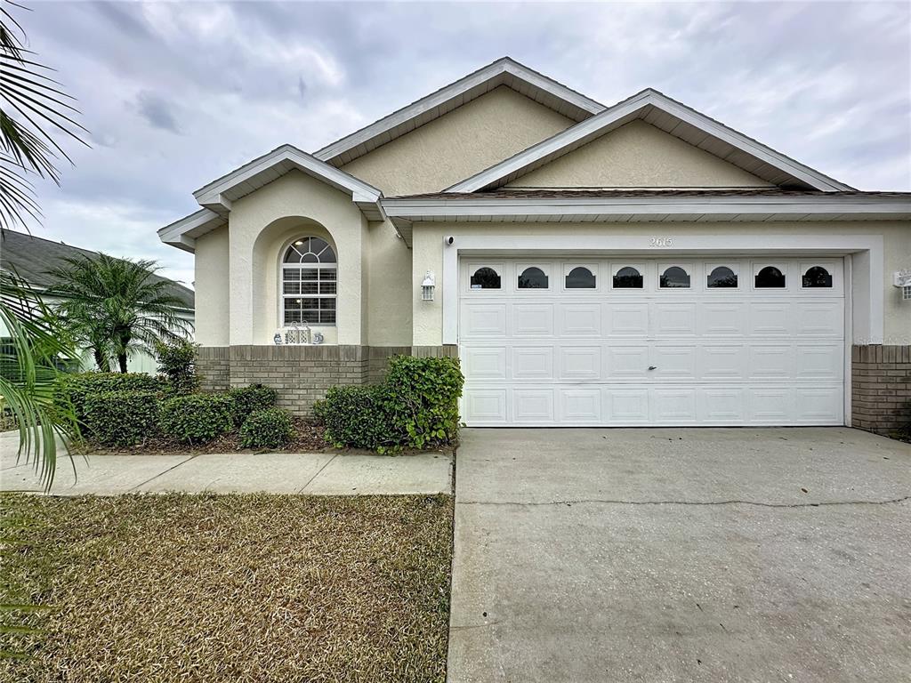 A single-story house with a white garage door, beige stucco walls, and a brick base — 2615 SUMMER CREEK DRIVE, KISSIMMEE, FL