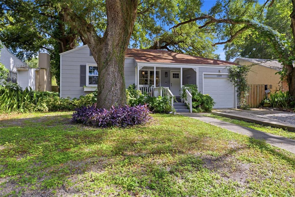 A single-story gray house with a front porch, a large tree, and a garage — 1209 E CRENSHAW STREET, TAMPA, FL