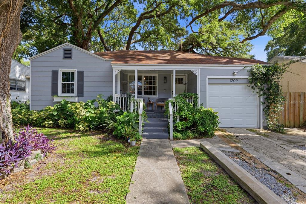 A single-story gray house with a front porch, attached garage, and mature trees — 1209 E CRENSHAW STREET, TAMPA, FL