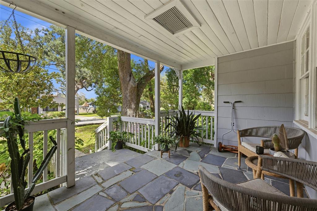A covered porch with a stone floor, white railings, and outdoor furniture overlooks a yard — 1209 E CRENSHAW STREET, TAMPA, FL