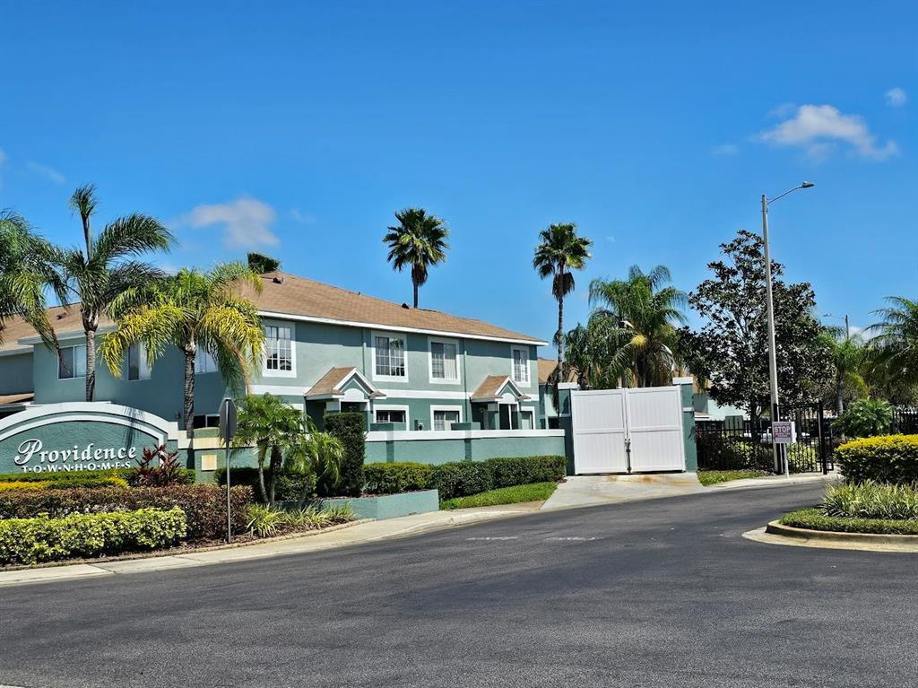 A two-story green townhouse complex features a gated entrance and palm trees under blue skies — 2053 FLUORSHIRE DRIVE, BRANDON, FL