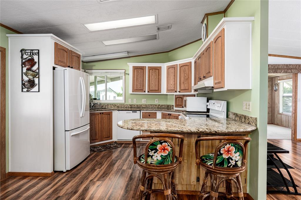 A kitchen features wood cabinets, granite countertops, a breakfast bar, and floral-patterned bar stools — 4215 14TH STREET E, ELLENTON, FL