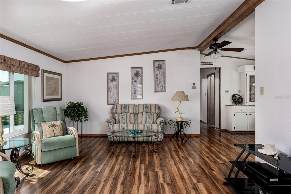 A living room features wood-look flooring, a patterned loveseat, a green recliner, and wall art — 4215 14TH STREET E, ELLENTON, FL