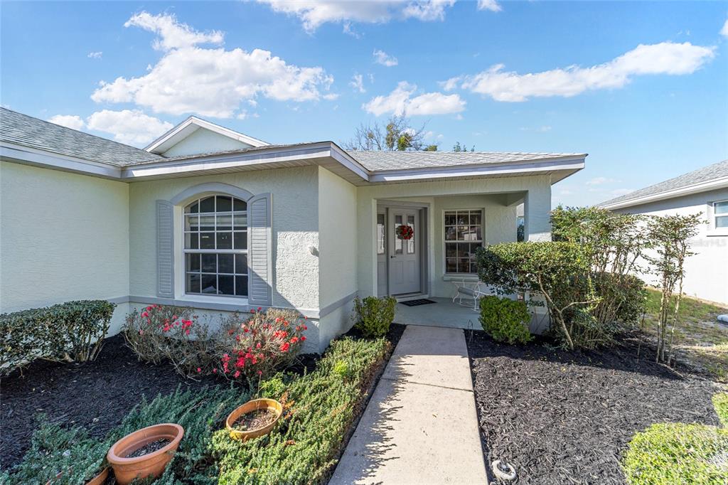 The exterior of a single-story house features a concrete walkway leading to a covered front entrance — 9686 SW 92ND PLACE ROAD, OCALA, FL