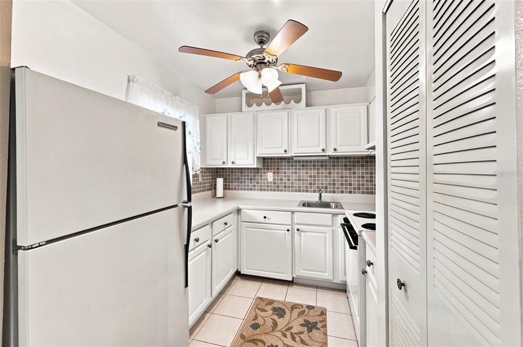 A white kitchen features a refrigerator, tiled backsplash, white cabinetry, and a ceiling fan — 2625 STATE ROAD 590 UNIT 1332, CLEARWATER, FL
