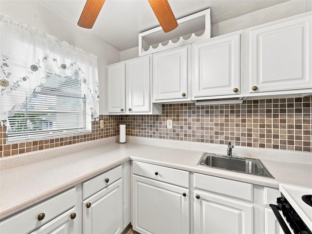 A kitchen with white cabinets, a brown tiled backsplash, and a stainless steel sink — 2625 STATE ROAD 590 UNIT 1332, CLEARWATER, FL