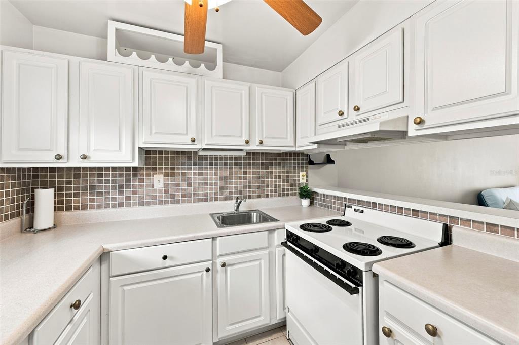 A kitchen features white cabinets, a tiled backsplash, a stainless steel sink, and white appliances — 2625 STATE ROAD 590 UNIT 1332, CLEARWATER, FL