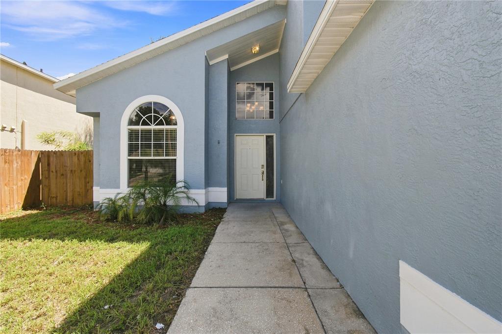 A blue house exterior features a concrete walkway leading to a white front door — 13417 BEECHBERRY DRIVE, RIVERVIEW, FL