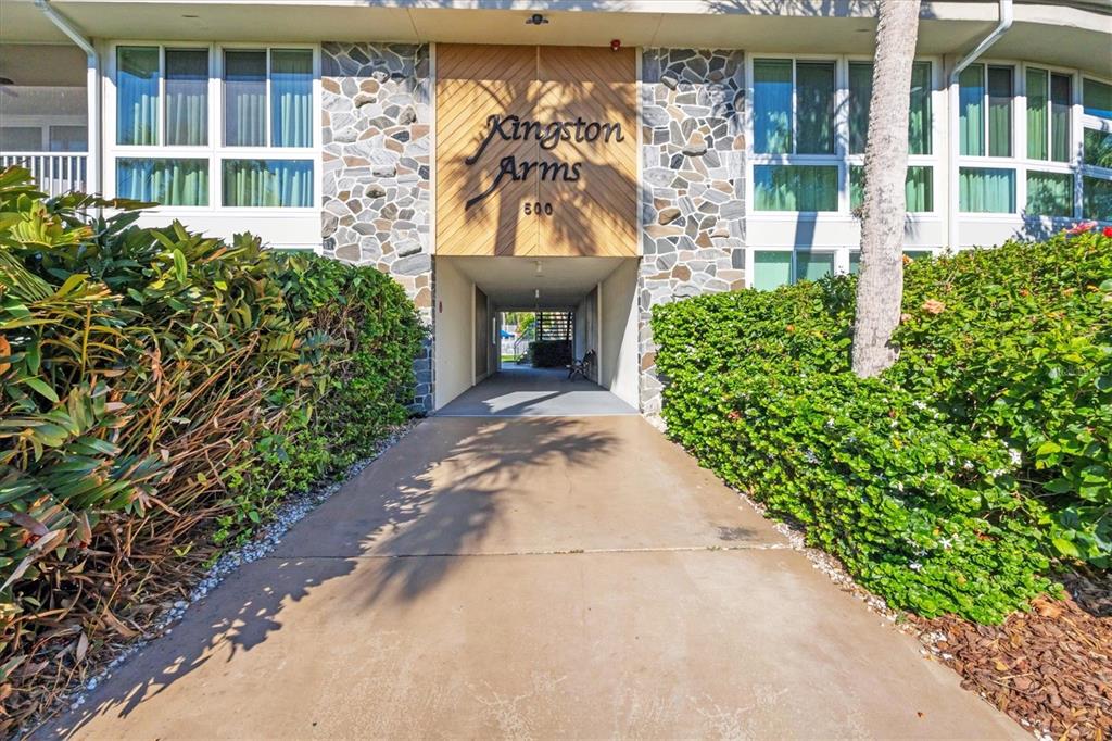The exterior of a multi-story building features a stone facade, wood paneling, and lush landscaping — 500 S WASHINGTON DRIVE UNIT 6B, SARASOTA, FL